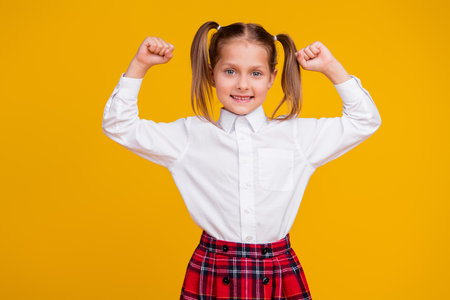 Portrait of little schoolkid raise fists wear uniform isolated on yellow color backgroundの写真素材
