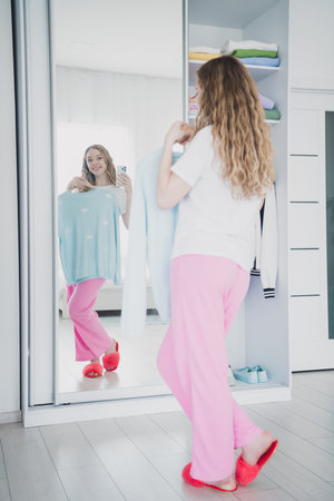 Vertical full length photo of teen blonde lady choose outfit mirror reflection selfie photo dressed sleepwear bedroom white light interiorの写真素材