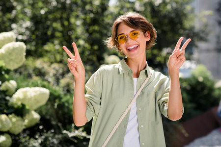 Photo of positive optimistic shiny girl rejoicing having fun good mood hands showing v-sign green...