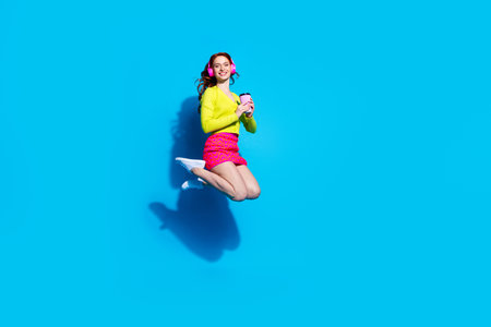 Full body photo of attractive young woman headphones jump drink coffee dressed stylish yellow...