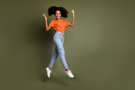 Full length photo of charming positive woman wear orange t-shirt jumping high empty space isolated...