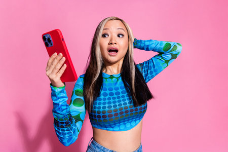 Photo of charming impressed woman wear blue top getting likes on a smartphone isolated pink color...