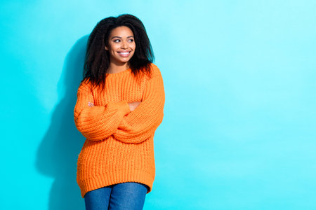 Photo of nice girl with perming coiffure dressed orange sweater arms crossed look at sale empty space isolated on teal color backgroundの写真素材
