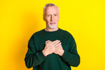 Photo portrait of handsome retired man hands touch chest heart health wear trendy green outfit isolated on yellow color backgroundの写真素材