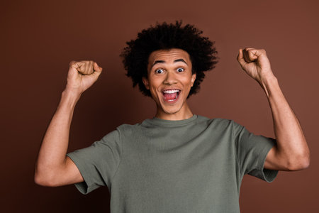 Photo of young guy with funny chevelure celebrate his successful bet played raised fists up isolated on brown color backgroundの写真素材