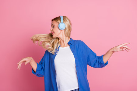 Portrait of carefree woman with fluttering wavy hair dressed blue shirt listen music in headphones isolated on pink color backgroundの写真素材