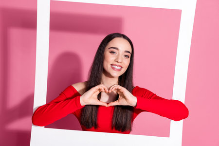 Photo of gorgeous young woman show heart symbol album card red shirt isolated on pink color...