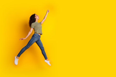Full size photo of positive girl dressed striped t-shirt jeans run look empty space hand catch object isolated on yellow color backgroundの写真素材