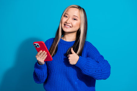 Photo portrait of teenager girl in stylish knitted sweater using mobile phone blogger thumb up like...