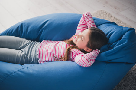 Photo portrait of cute adorable girl daughter sit bean bag relaxed hands behind head remote lesson education from home indoorsの写真素材
