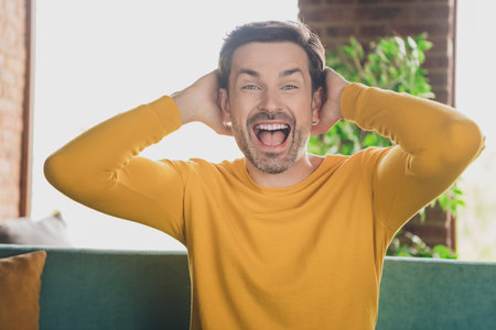 Photo of young speechless impressed man staying home sitting on comfortable couch loves being domestic spend time having fun watch tvの写真素材
