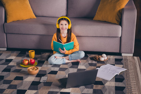Full size photo of small girl sit floor do homework snack netbook video call dressed orange outfit...