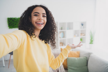 Self portrait of happy positive young american girl wearing yellow shirt demonstrate modern design furniture renovation at homeの写真素材