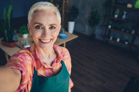 Photo portrait of pretty senior female professional florist take selfie photo smile wear apron working flower shop deliveryの写真素材