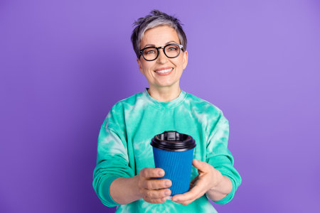 Photo portrait of attractive senior woman drink coffee hold paper cup dressed stylish green clothes isolated on purple color backgroundの写真素材