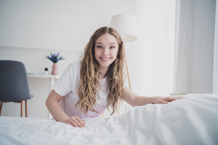Full body photo of sweet pretty teen girl cheerful making bed morning routine wear pajama white interior bedroom apartmentの写真素材