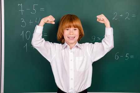 Photo of cute little schoolboy diligent show muscles achievement winning dressed stylish uniform classroom blackboard backgroundの写真素材