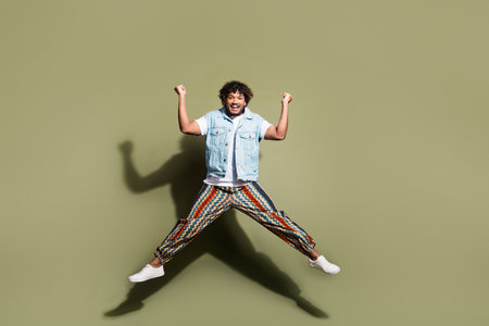 Full size photo of handsome young guy jump winning wear trendy jeans outfit isolated on khaki color backgroundの写真素材