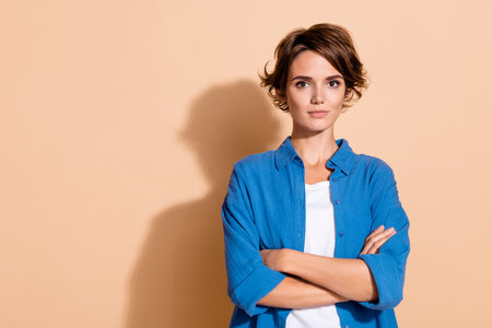 Portrait of senior level backend developer young woman in blue shirt folded hands poses at office isolated on beige color backgroundの写真素材