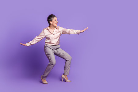 Full size photo of nice pensioner female keep balance surfing wear trendy satin outfit isolated on violet color backgroundの写真素材