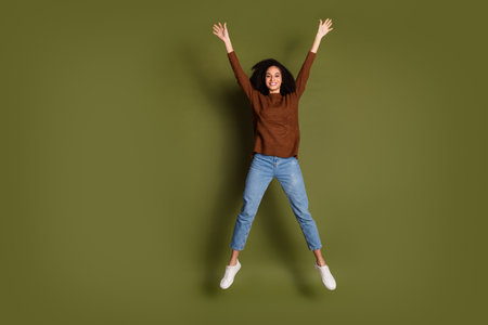 Full length portrait of pretty young woman jump empty space wear sweater isolated on khaki color...