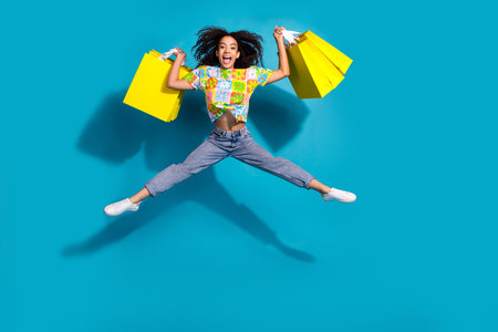 Full length photo of cheerful pretty lady dressed flower print t-shirt jumping rising bargains empty space isolated blue color backgroundの写真素材