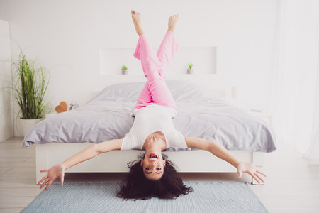 Full body photo of upside down american teenager overjoyed carefree girl laying on bed in sleepwear wake up cozy bedroom indoorsの写真素材