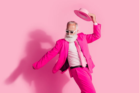 Photo of attractive elderly white hair santa man mc showman sunglass dance hold hat wear stylish pink suit isolated over pastel backgroundの写真素材