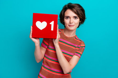 Portrait of satisfied girl blogger with short hairstyle wear stylish shirt hold one social media like isolated on teal color backgroundの写真素材