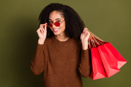 Portrait of pretty young woman touch sunglass hold bags wear sweater isolated on khaki color backgroundの写真素材