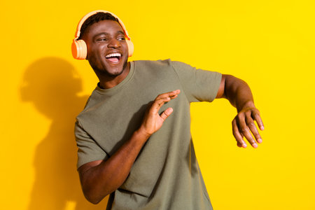Photo of cheerful positive man wear trendy khaki clothes listen music look empty space isolated on yellow color backgroundの写真素材