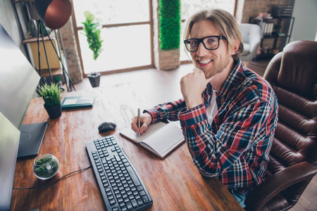 Photo of handsome young guy minded write notebook working study wear plaid shirt coworking successful businessman nice light officeの写真素材