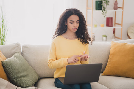 Photo portrait of wavy hair young girl sitting and studying from home using her laptop learning count maths indoors living room apartmentの写真素材