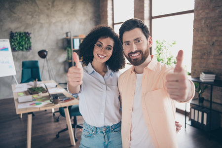Photo of two young colleagues embrace demonstrate thumb up loft interior office business center...