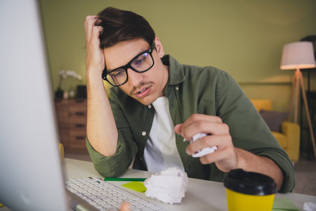 Photo of stressed depressed adult man sit table work from home interior room workplace workspace evening light indoorsの写真素材