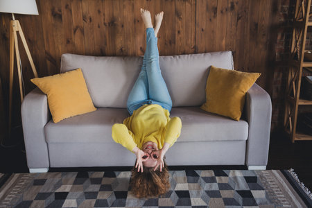 Full length photo of young lady lying sofa upside down binoculards eyes dressed yellow sweater spend pastime spacious house indoors roomの写真素材