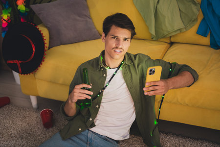 Photo of funny guy feeling bad after party celebration holding gadget indoors room home house...