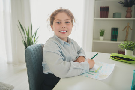 Photo of cheerful cute adorable girl dressed uniform sitting chair art lesson home education daylight indoorsの写真素材