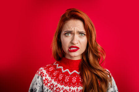 Portrait photo of young lady guilty biting lips wearing ugly sweater celebrating christmas holiday isolated on red color backgroundの写真素材