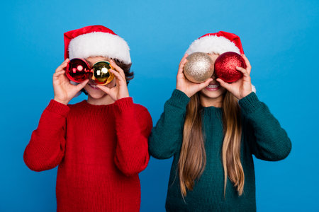 Photo of two people kids close eyes with christmas tree balls isolated blue color backgroundの写真素材