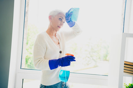 Photo of adorable charming lovely retired woman wear cardigan wipe window glass weekend spring cleaning indoors room home houseの写真素材