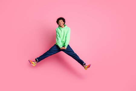 Full body portrait of cool young man jump empty space wear green hoodie isolated on pink color backgroundの写真素材