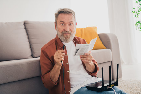 Photo of senior male sit couch sit floor confused fix wifi router dressed brown outfit cozy day...