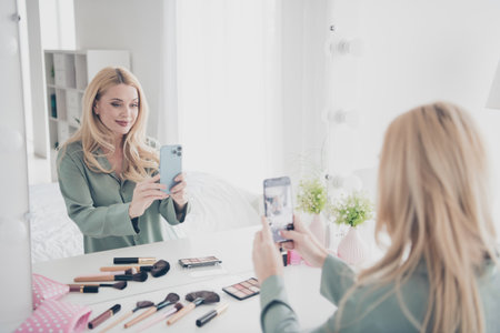 Portrait of nice young lady smart phone mirror selfie silky pajama white interior bedroom flat indoorsの写真素材