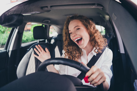 Photo of cheerful pretty lady dressed white shirt singing driving automobile enjoy traffic outdoors urban city streetの写真素材