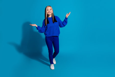Full length body photo funny youngster trendy japanese girl in fall season outfit and white sneakers isolated on blue color backgroundの写真素材