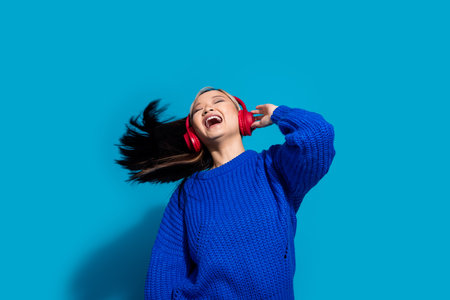 Photo portrait of japanese funky chilling girl shaking head rhythm music lover in headphones isolated on blue color backgroundの写真素材