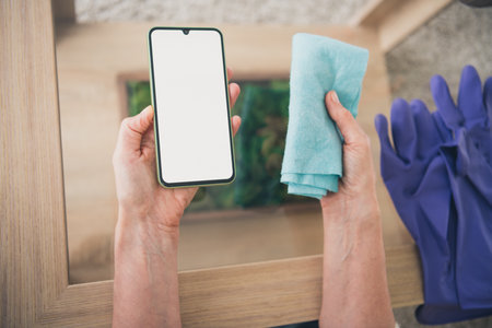 Cropped above view portrait of lady hands hold cleaning rug empty space smart phone screen living...