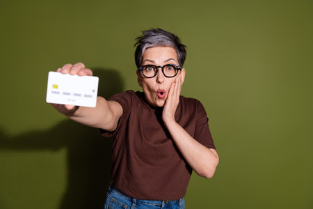 Portrait of pretty aged lady hold show credit card wear brown t-shirt isolated on khaki color backgroundの写真素材
