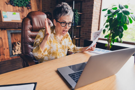 Photo of angry mad crazy senior lady sitting armchair work modern loft interior indoors workstation workspaceの写真素材